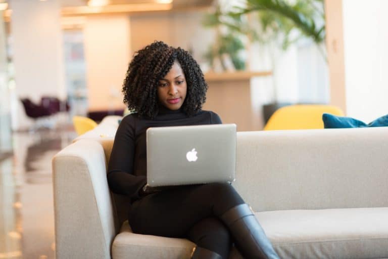 Woman working on a laptop while sitting on a sofa in a bright office lounge