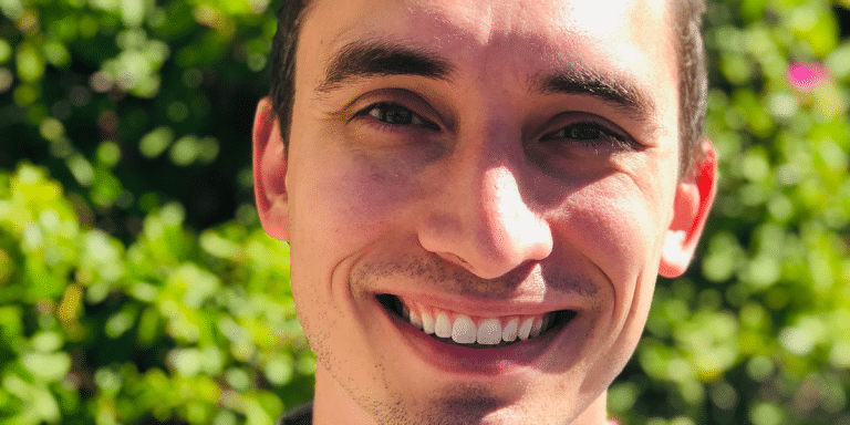 Headshot of recruiter Aaron Mullenix smiling in front of green foliage