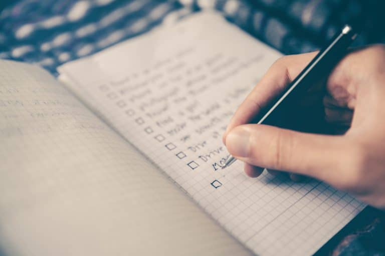 Hand ticking items on a handwritten checklist in a grid notebook