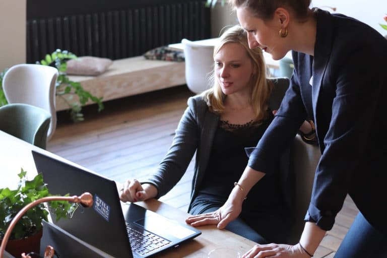 Two women looking at a laptop together, one standing and pointing at the screen