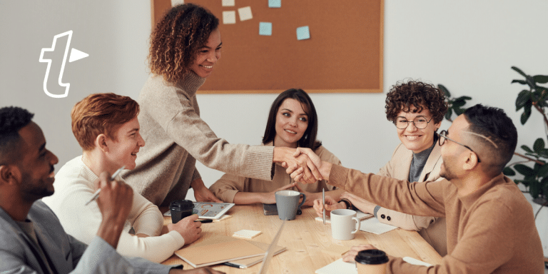 team sat at desk with two people shaking hands