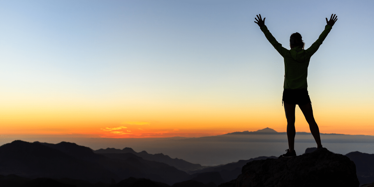 man with arms up on top on mountain