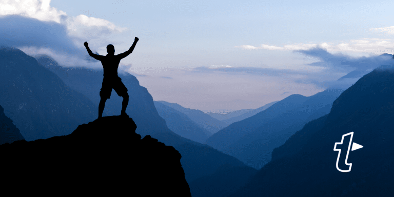 Silhouette of a person celebrating with arms raised on a mountain peak, with the TextExpander logo