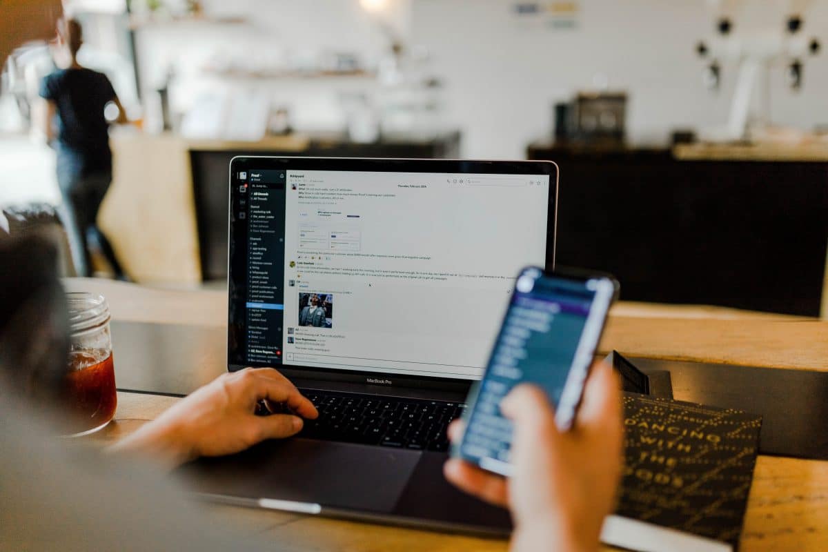 Photo of someone working on their laptop while using their cell phone. 