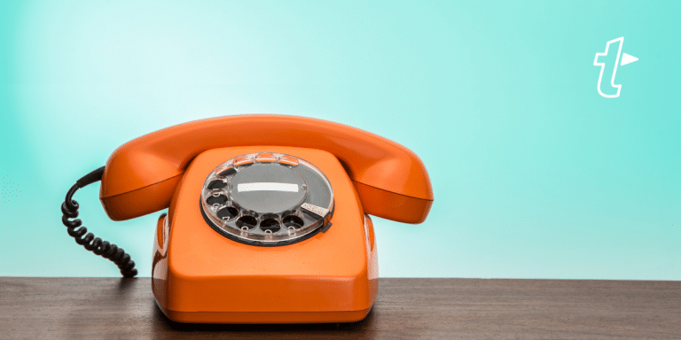 Bright orange rotary telephone on a wooden table against a teal background