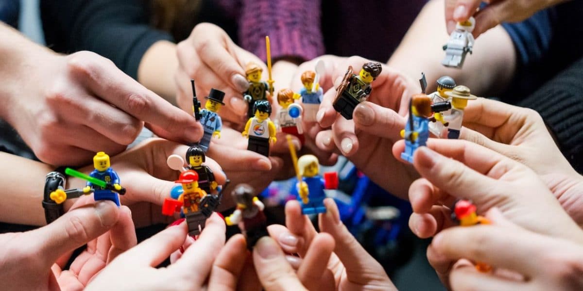 Many hands holding up LEGO minifigures together, suggesting a team
