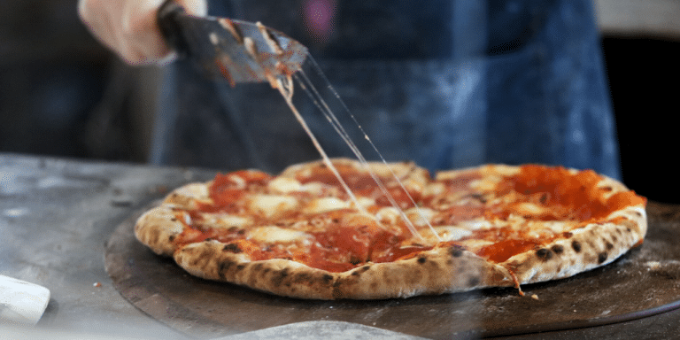 Pizza being sliced on a peel, with cheese stretching from the cutter
