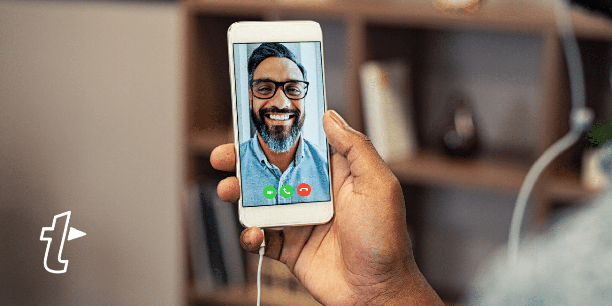 Hand holding a smartphone on a video call with a smiling bearded man, with the TextExpander logo