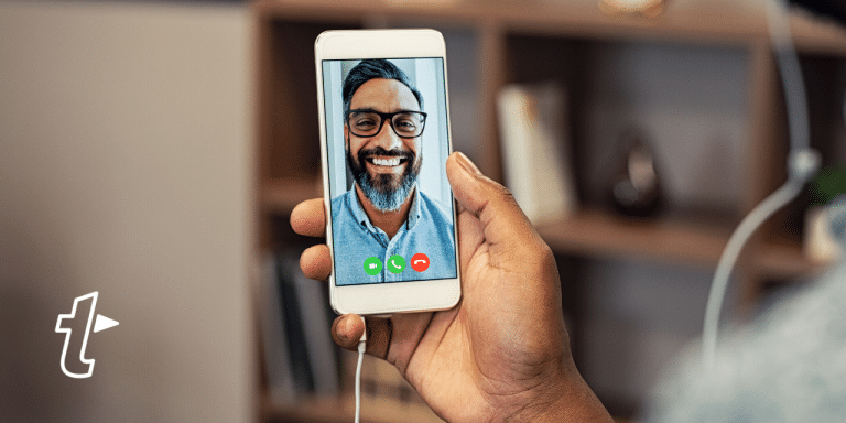 Hand holding a smartphone on a video call with a smiling bearded man, with the TextExpander logo