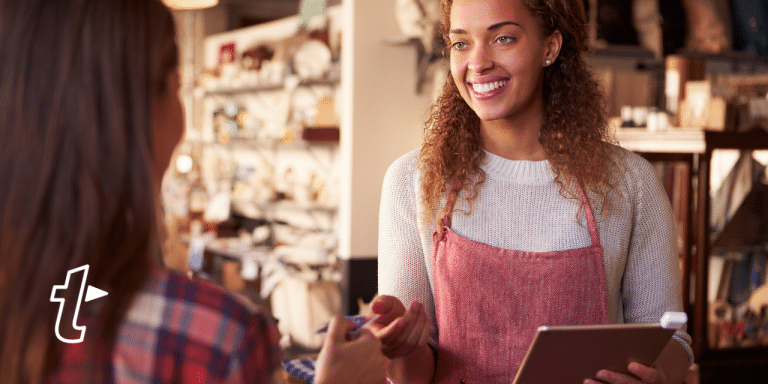 Smiling shop assistant in an apron holding a tablet while serving a customer