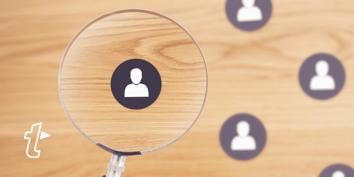 Magnifying glass focuses on one person icon among several on a wooden surface, illustrating finding the right sales prospects