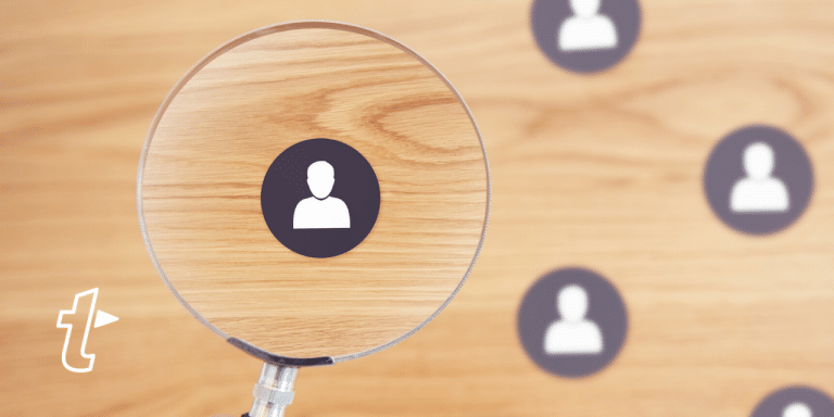 Magnifying glass focuses on one person icon among several on a wooden surface, illustrating finding the right sales prospects