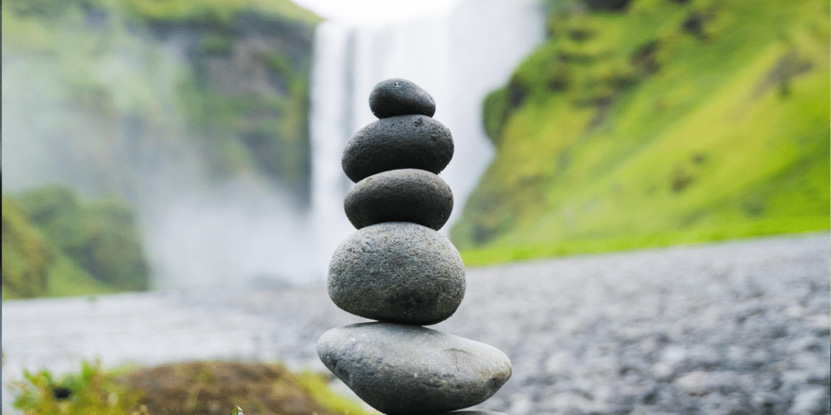 Stack of balanced smooth stones in front of a misty waterfall and green hillside