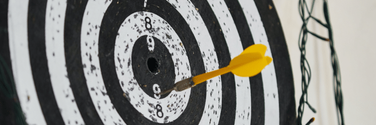 Yellow dart stuck in a black and white dartboard just off the bullseye