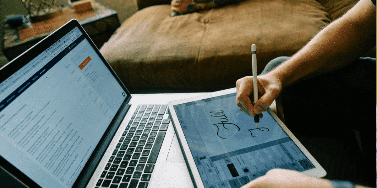 Person writing with a stylus on a tablet beside a laptop