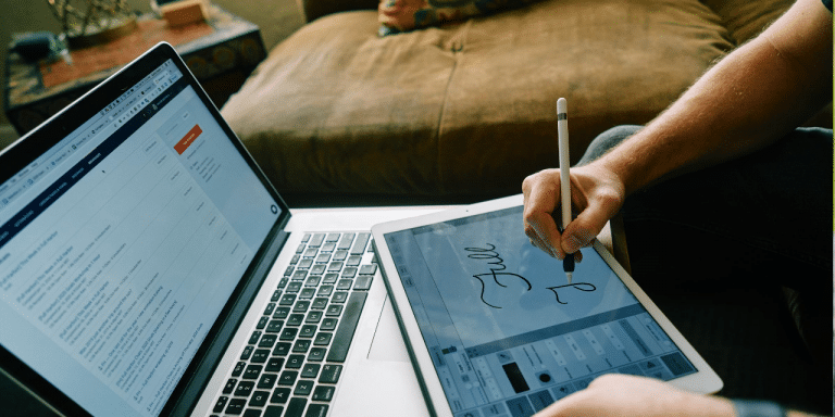 Person writing with a stylus on a tablet beside a laptop