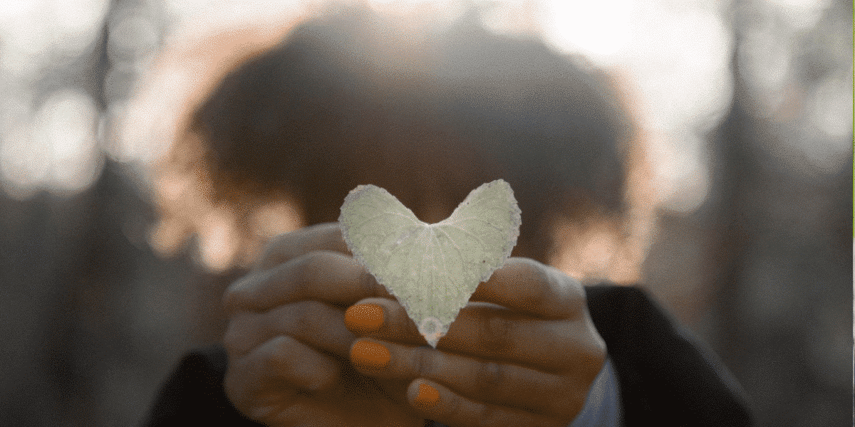 Person holding a heart-shaped leaf in front of their face