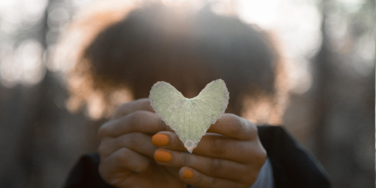 Person holding a heart-shaped leaf in front of their face