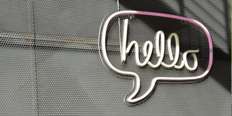 Neon hello sign inside a speech bubble on a perforated metal wall