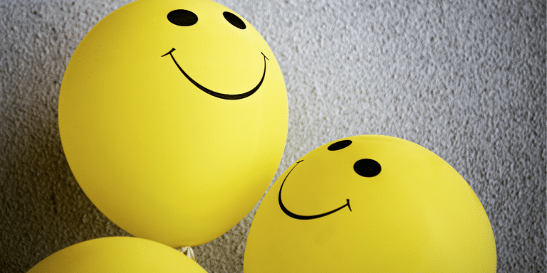 Yellow smiley-face balloons against a textured grey wall