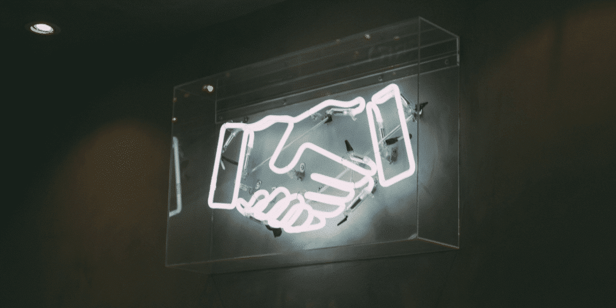 Neon sign of a handshake glowing on a dark wall
