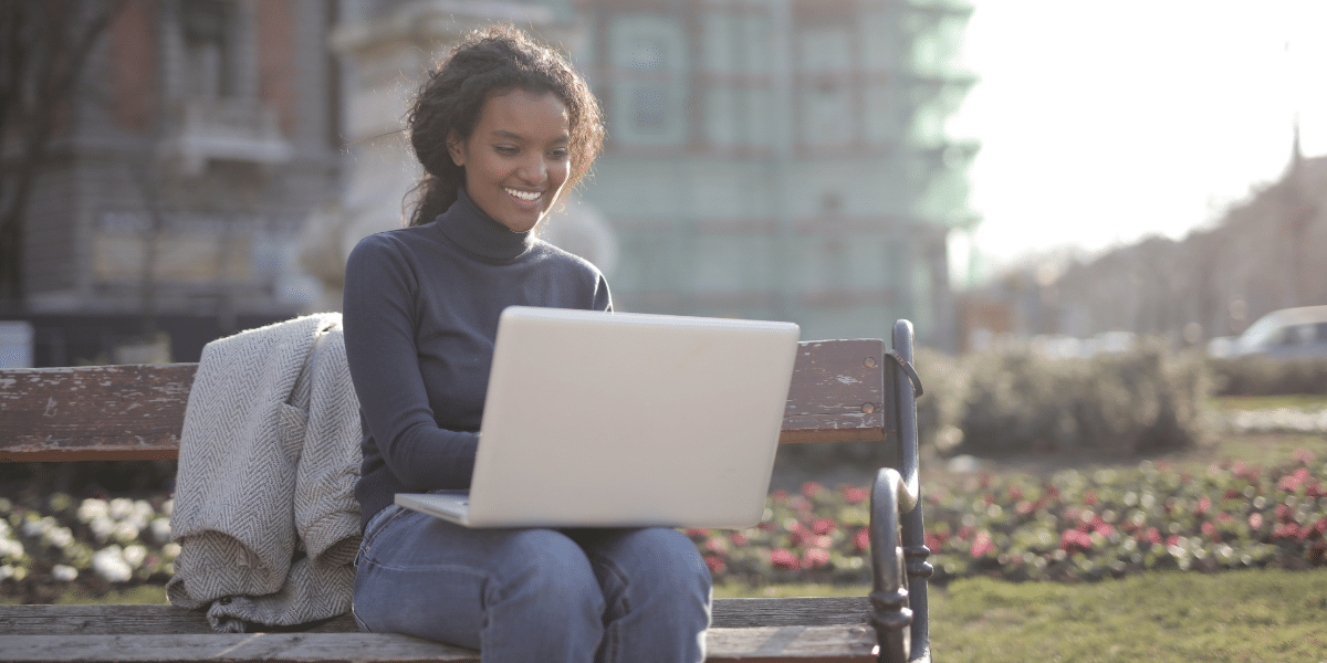 smiling woman on park bench with laptop