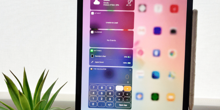 iPad on a desk showing the Today View widgets, including calendar, batteries and a calculator, beside a potted plant