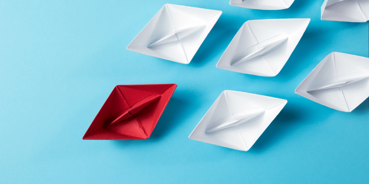 red paper boat leading white paper boats
