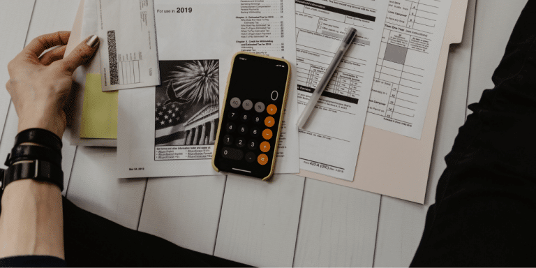 Overhead view of tax forms, a calculator app on a phone and a pen on a desk, suggesting a review or audit