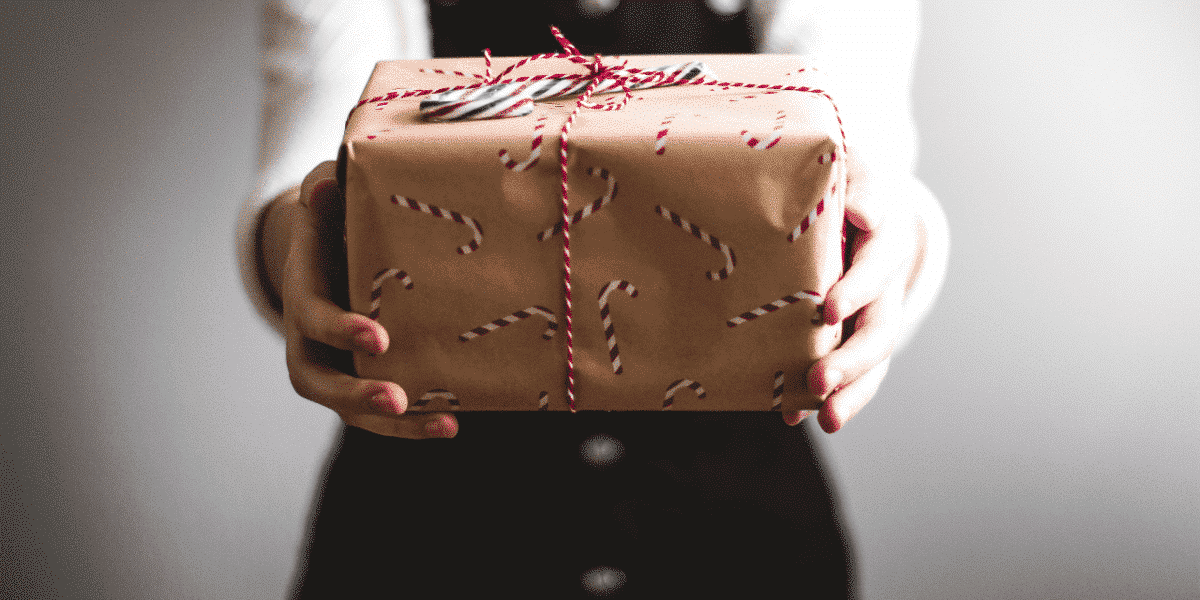 Hands holding out a gift wrapped in candy-cane paper and red-and-white string