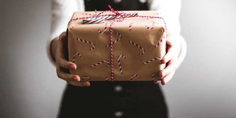 Hands holding out a gift wrapped in candy-cane paper and red-and-white string