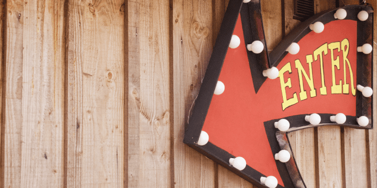 Red arrow-shaped marquee sign reading "Enter" on a wooden wall