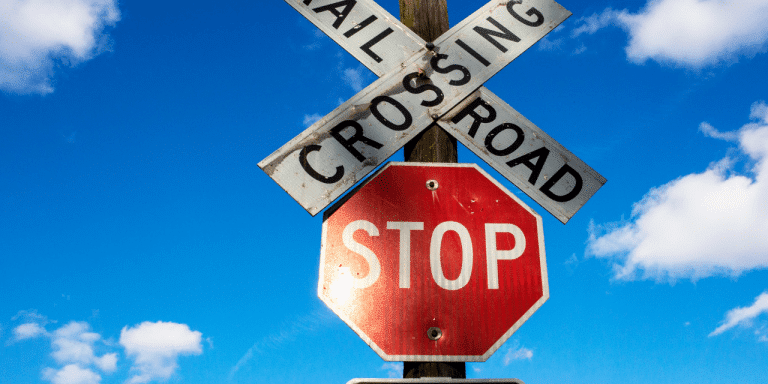 Railroad crossing sign above a red stop sign against a blue sky