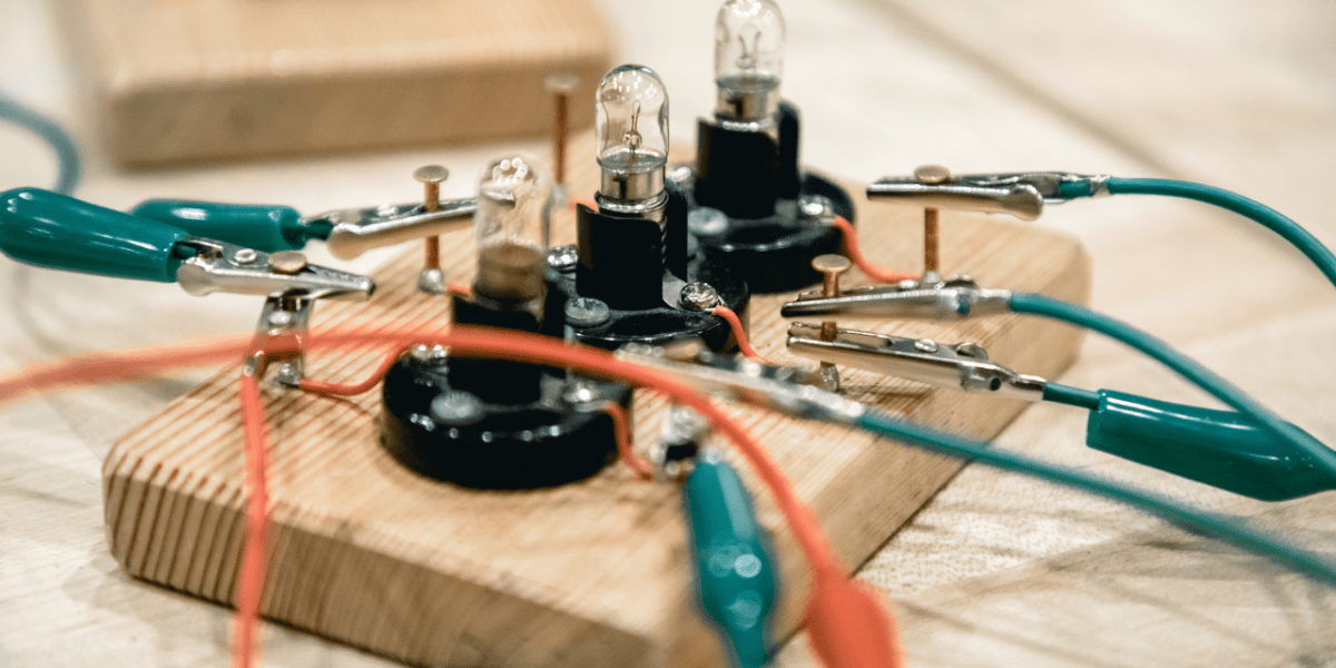 Simple circuit with light bulbs on a wooden board connected by alligator-clip wires, symbolising connection