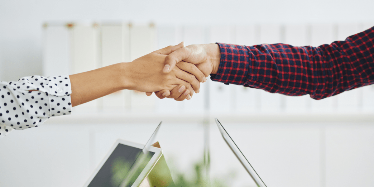 Two people shaking hands, with only their arms & hands in view.