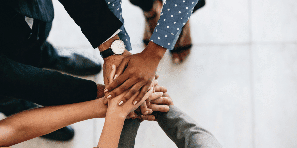 3 people with their hands put into the middle, in a circle, suggesting teamwork