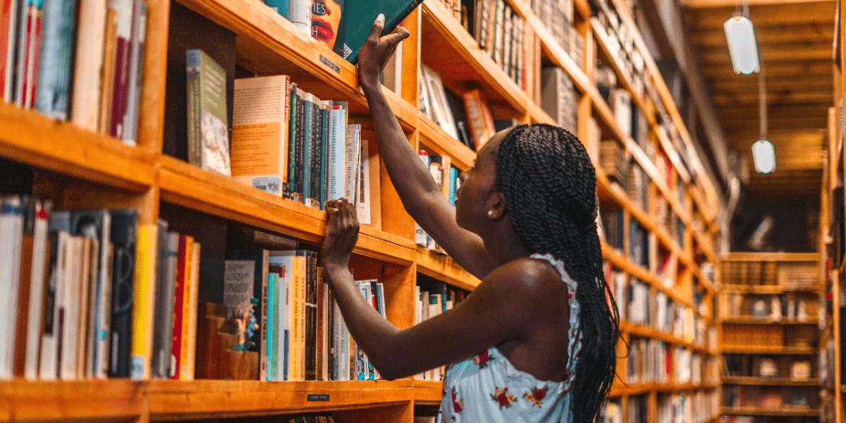 A woman pulling out a book from a high shelf in a library