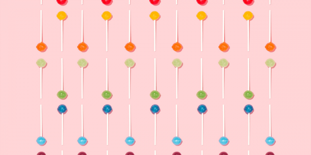 Multicoloured lollipops laid out neatly in lines on a bright pink background.
