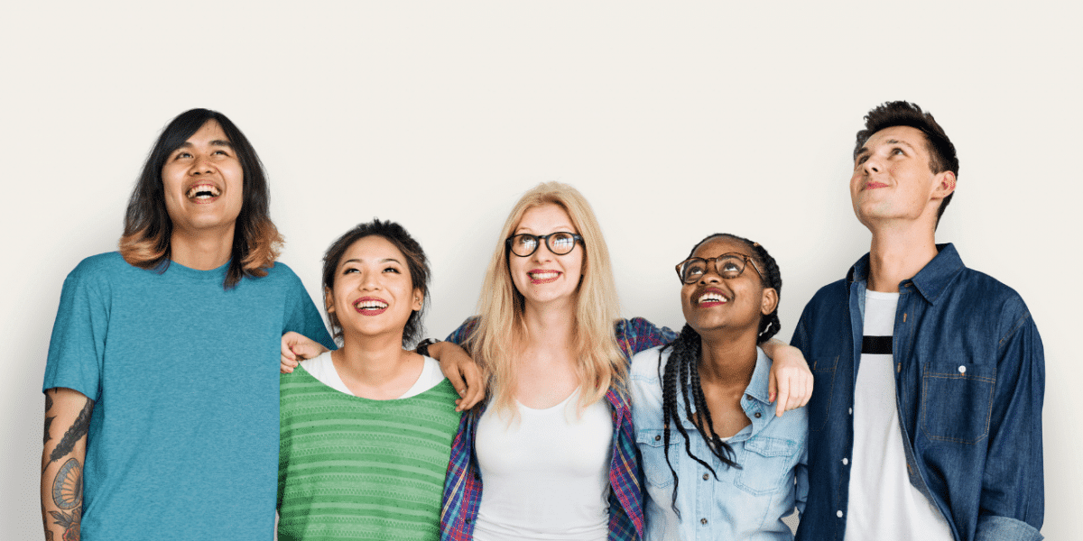 5 young people of mixed culture and age with their arms around each other's shoulders, looking up
