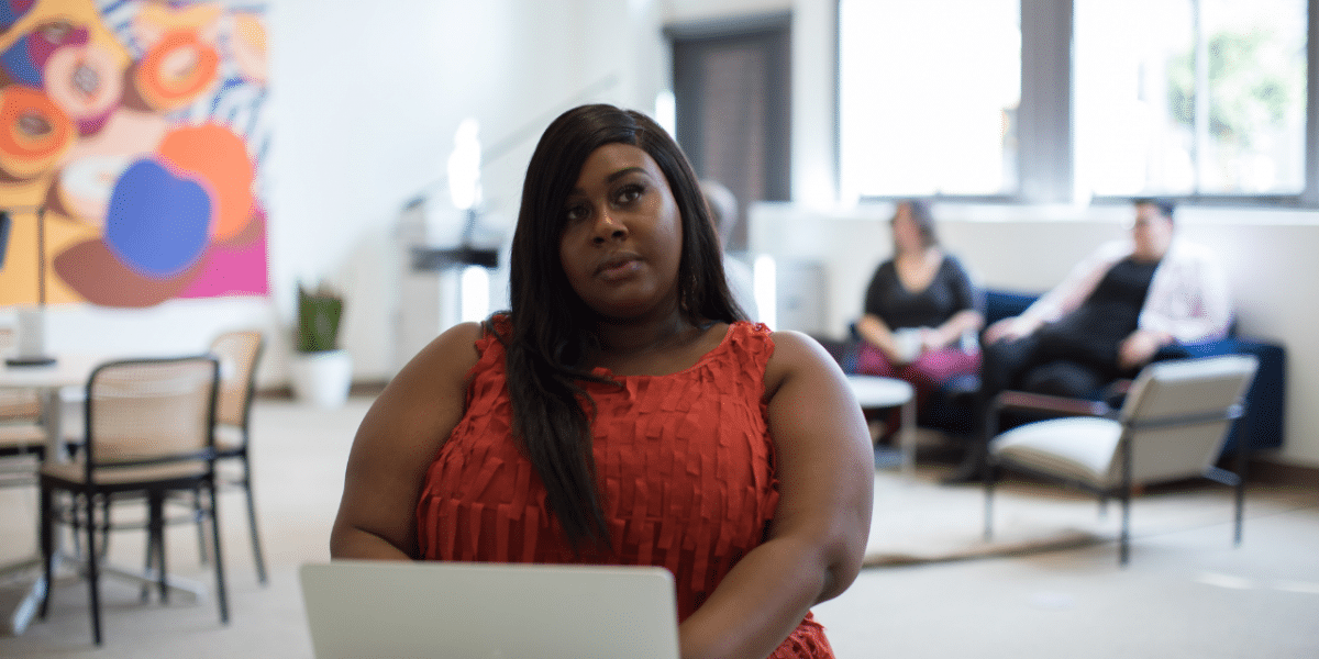 Woman in a red top sitting with a laptop in a bright open office