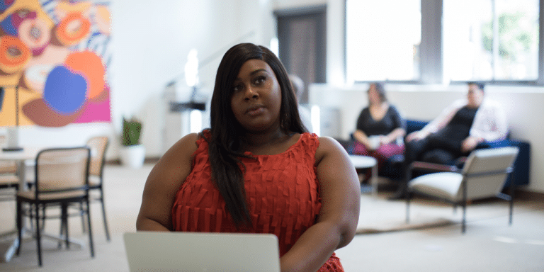 Woman in a red top sitting with a laptop in a bright open office