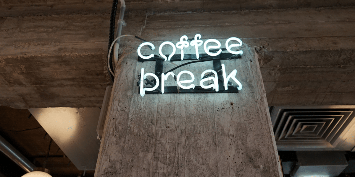 A blue-ish white neon sign against an industrial wall reading 'COFFEE BREAK'