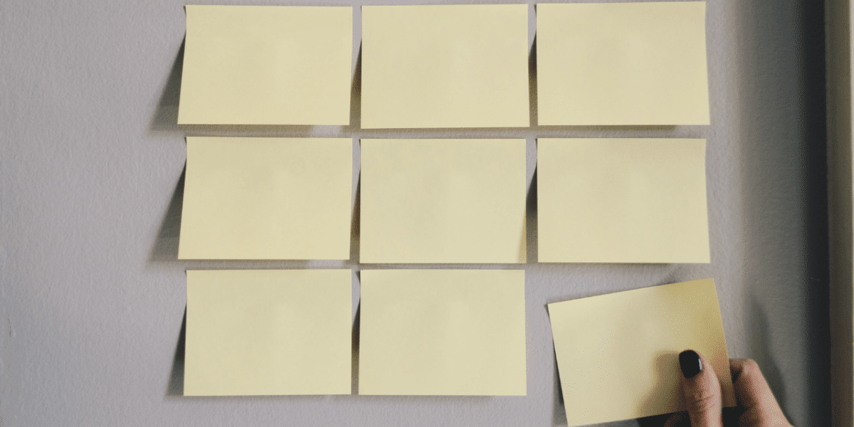 Yellow post-it notes lined up on a wall. A hand is in the process of putting another one up