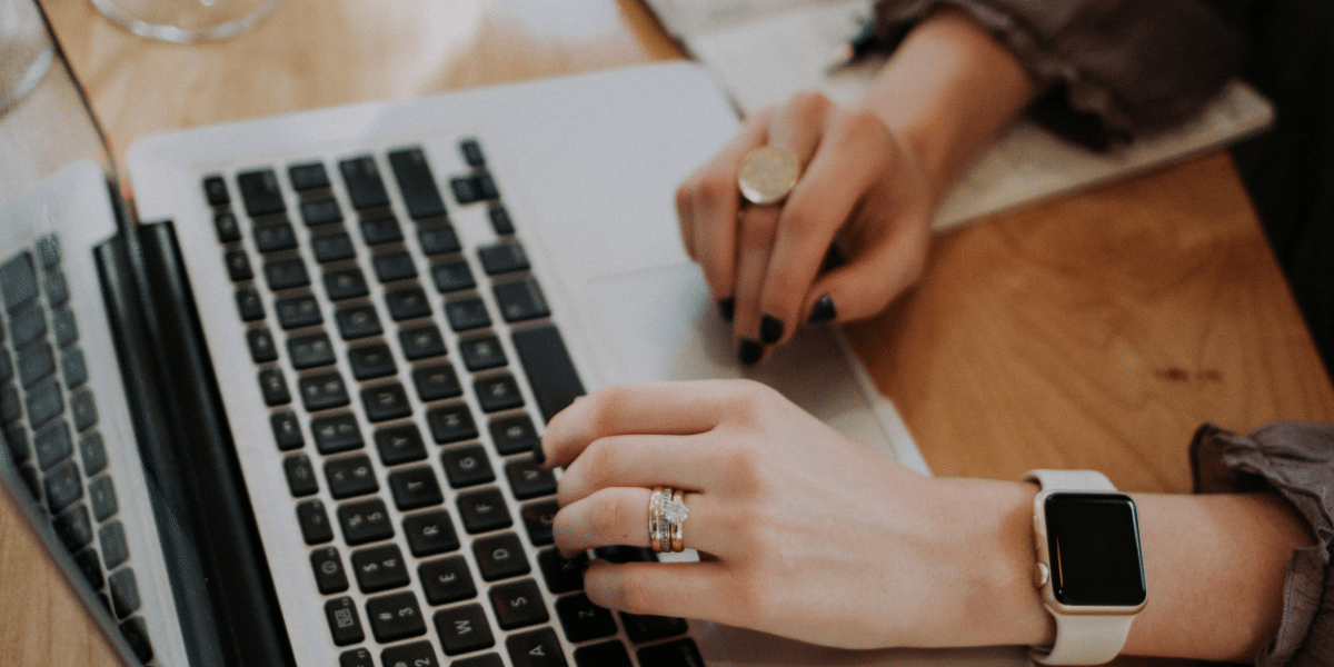 A woman typing on a laptop. The image only shows her hands on the laptop keyboard.