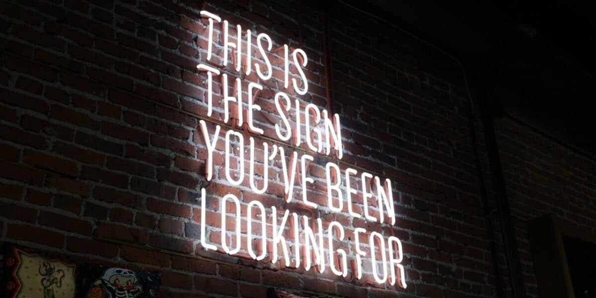 A large pale pink neon light reading 'THIS IS THE SIGN YOU'VE BEEN LOOKING FOR'