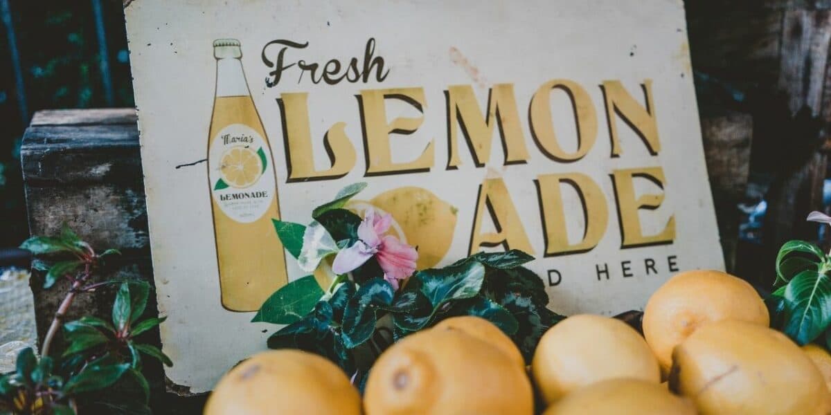 A sign reading 'fresh lemonade sold here' with a pile of lemons in front of it