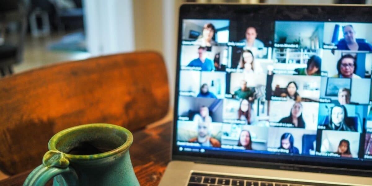 A laptop with a video call full of people slightly out of focus, while a green coffee cup is in focus in the foreground