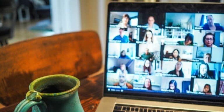A laptop with a video call full of people slightly out of focus, while a green coffee cup is in focus in the foreground