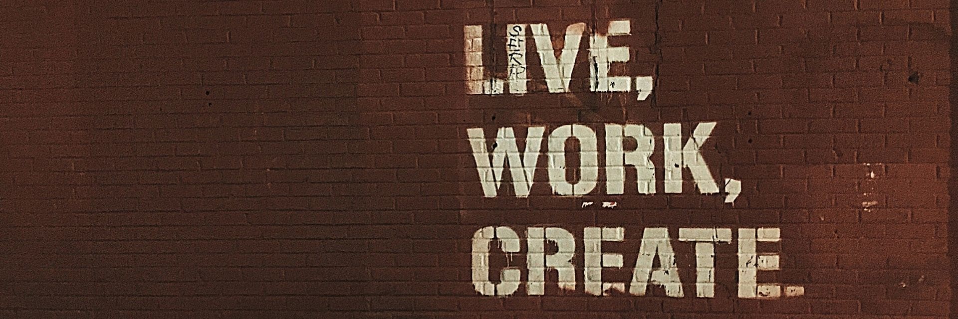 A red brick wall with white, bold painted words, reading "LIVE, WORK, CREATE"