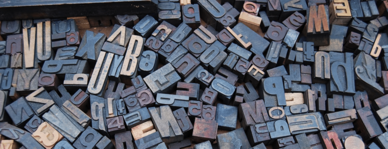 Pile of vintage wooden letterpress type blocks, representing predictive text and typing